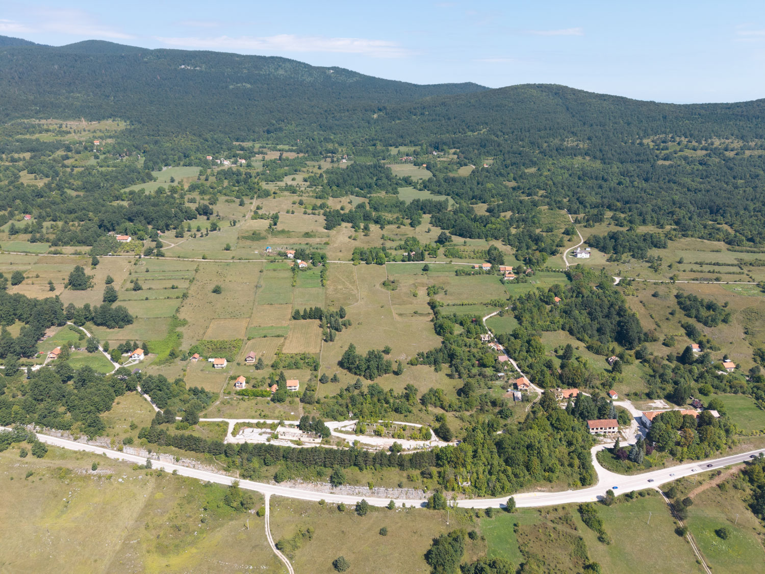 Razloženi naselji Jasenovac (levo) in Bravsko (desno). Vhod v brezno je na pobočju sredini na začetku strnjenega gozdnega roba.
